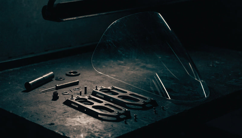 Motorcycle windscreen and mounting hardware laid out on a workshop bench